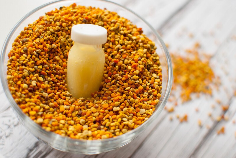 This photo shows a bowl of bee pollen with a tiny jar of light honey in it on a wooden table.