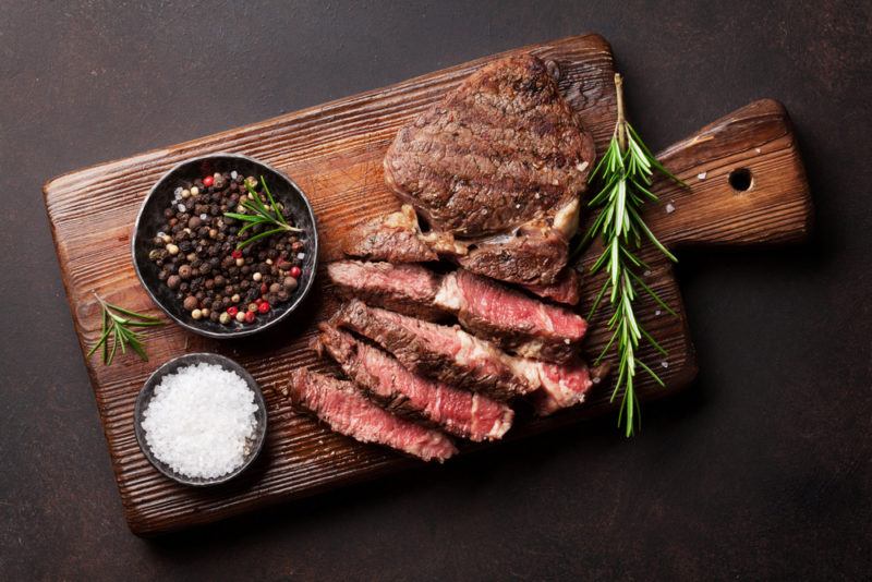 A cooked steak on a cutting board, with various slices