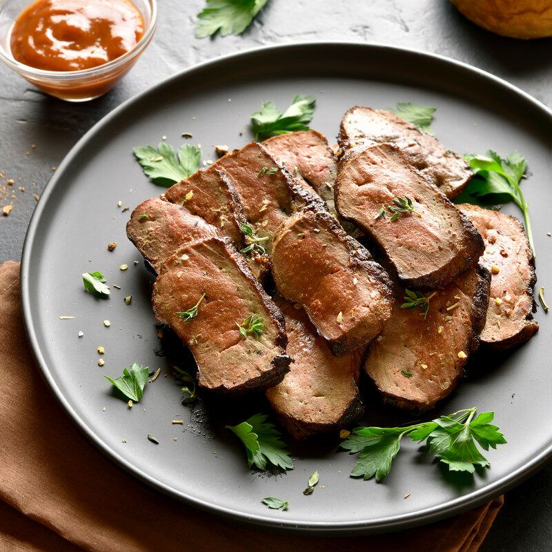 This photo shows several cuts of cooked beef liver on a dark plate with parsley sprigs.