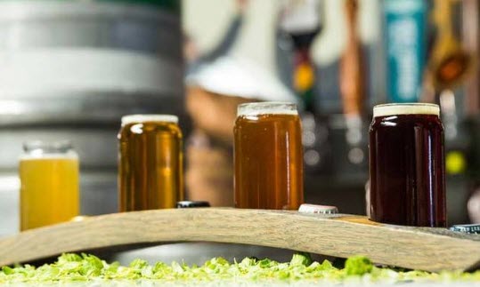 Wooden beer flight with 4 different colored glasses of beer and bottle caps. 