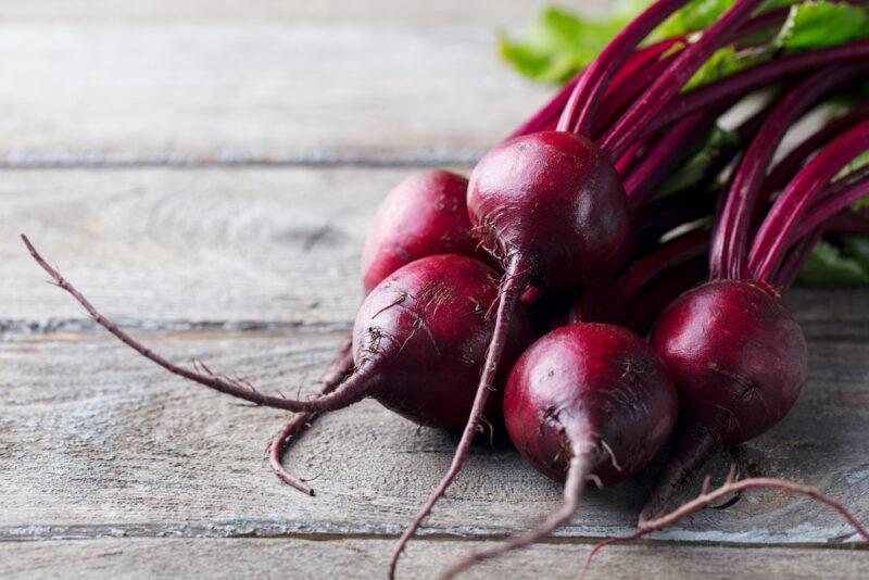 A bunch of dark red beets rests on a wooden surface.