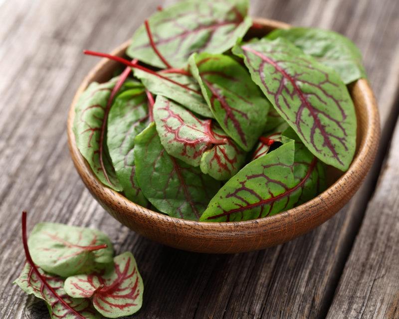 A bowl of beet greens on a wooden table