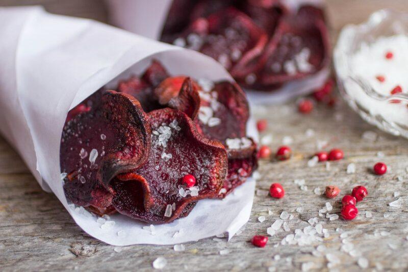 A wrapped white piece of paper with beetroot chips, salt, and pepper