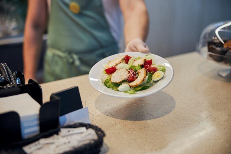 A woman handing a white plate with a salad to a customer at an airport