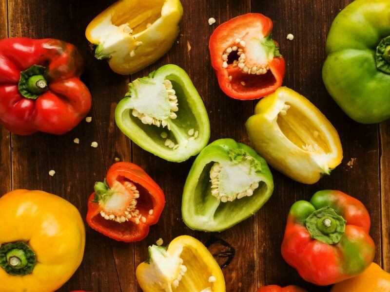 A selection of bell peppers on a wooden table. A few of them are whole, while the rest have been cut in half