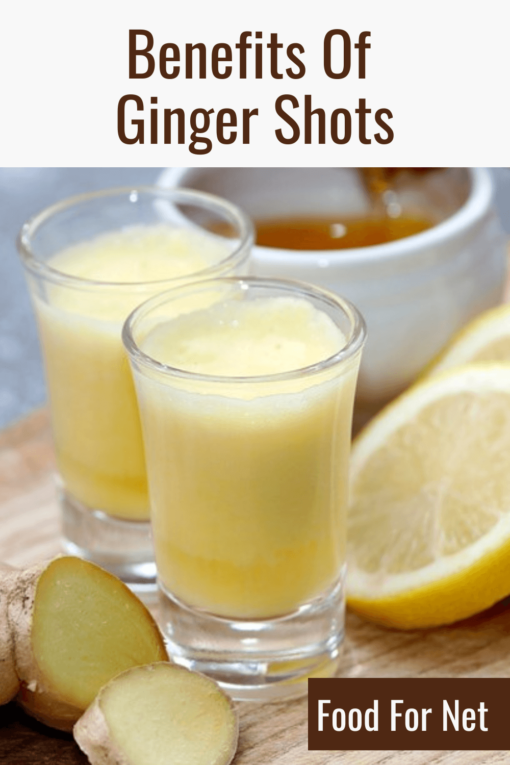 A wooden tray with two ginger shots, some ginger root, honey, and lemons, highlighting the benefits of ginger shots