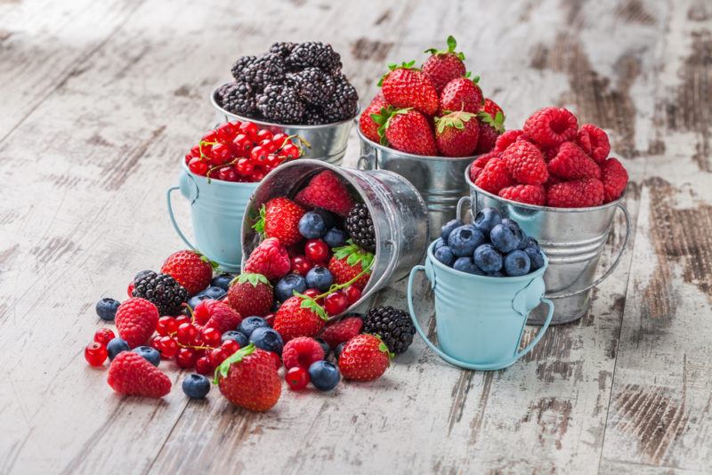 Various small metal pails and cups filled with different berries