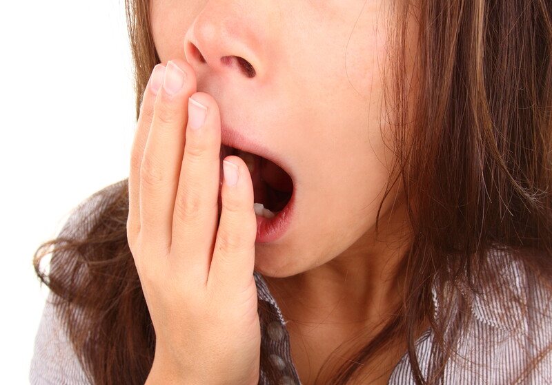 Best Foods Fatigue | Food For Net This photo shows a dark-haired woman yawning behind her hand, representing the best foods for fatigue.