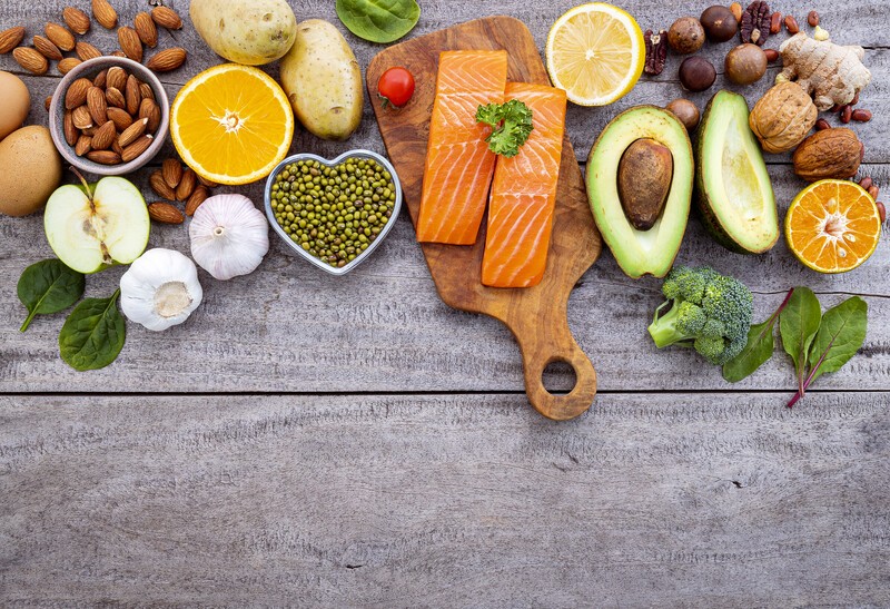 This photo shows an overhead view of several diabetic-friendly foods on a wooden table, including avocado, salmon, lemon, garlic, almonds, eggs, and more, representing the best foods for diabetes.