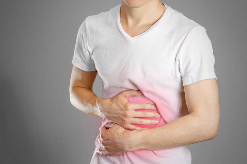 A man in a white tee shirt holds his stomach, which glows red through his shirt to indicate pain, with both hands, representing the best foods for gastroparesis.