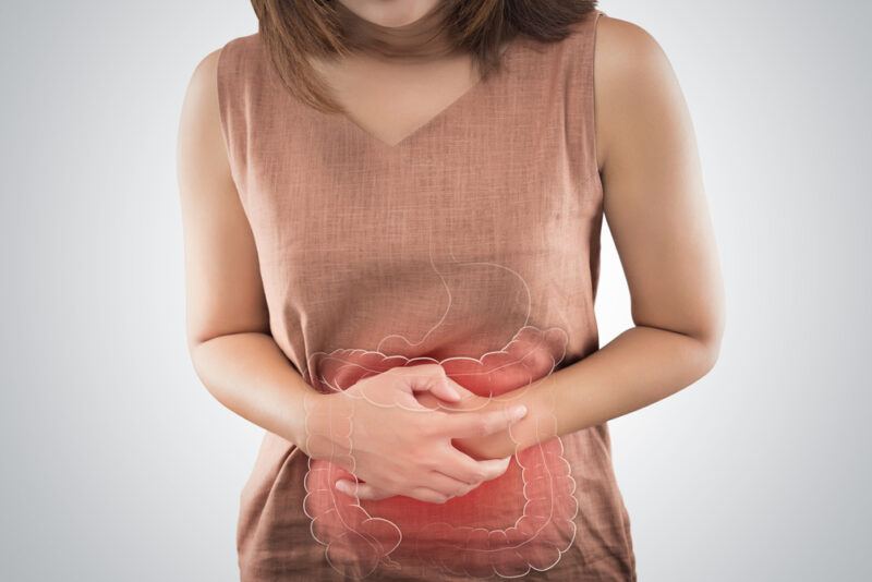 The,Photo,Of,Large,Intestine,Is,On,The,Woman's,Body. | Food For Net This photo shows a brunette woman in a brown shirt holding her stomach, with an overlay image showing an inflamed large intestine, representing the best foods for irritable bowel syndrome.