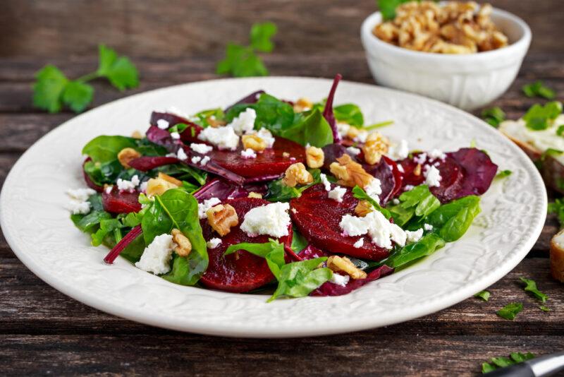 This photo shows a white plate with a salad containing walnuts, beets, and spinach, representing the best foods to eat for nitric oxide.