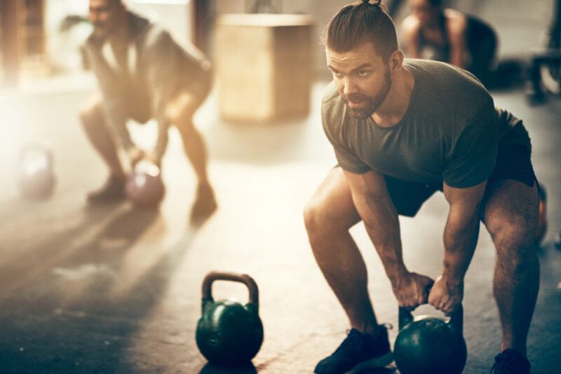 A man in a tee shirt and shorts squats over a kettlebell, representing the best foods for working out.