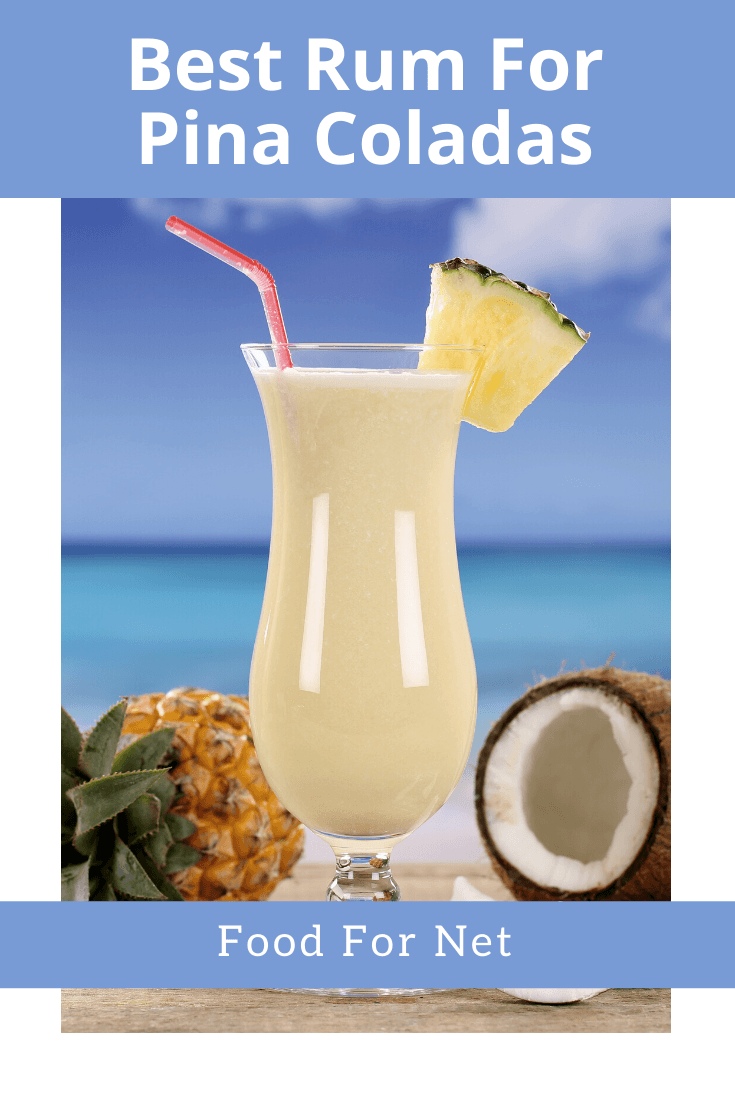 A glass of pina colada in front of an ocean next to a pineapple and coconut