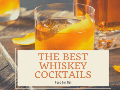 A whiskey cocktail in the foreground with another in the background, with a bottle of whiskey