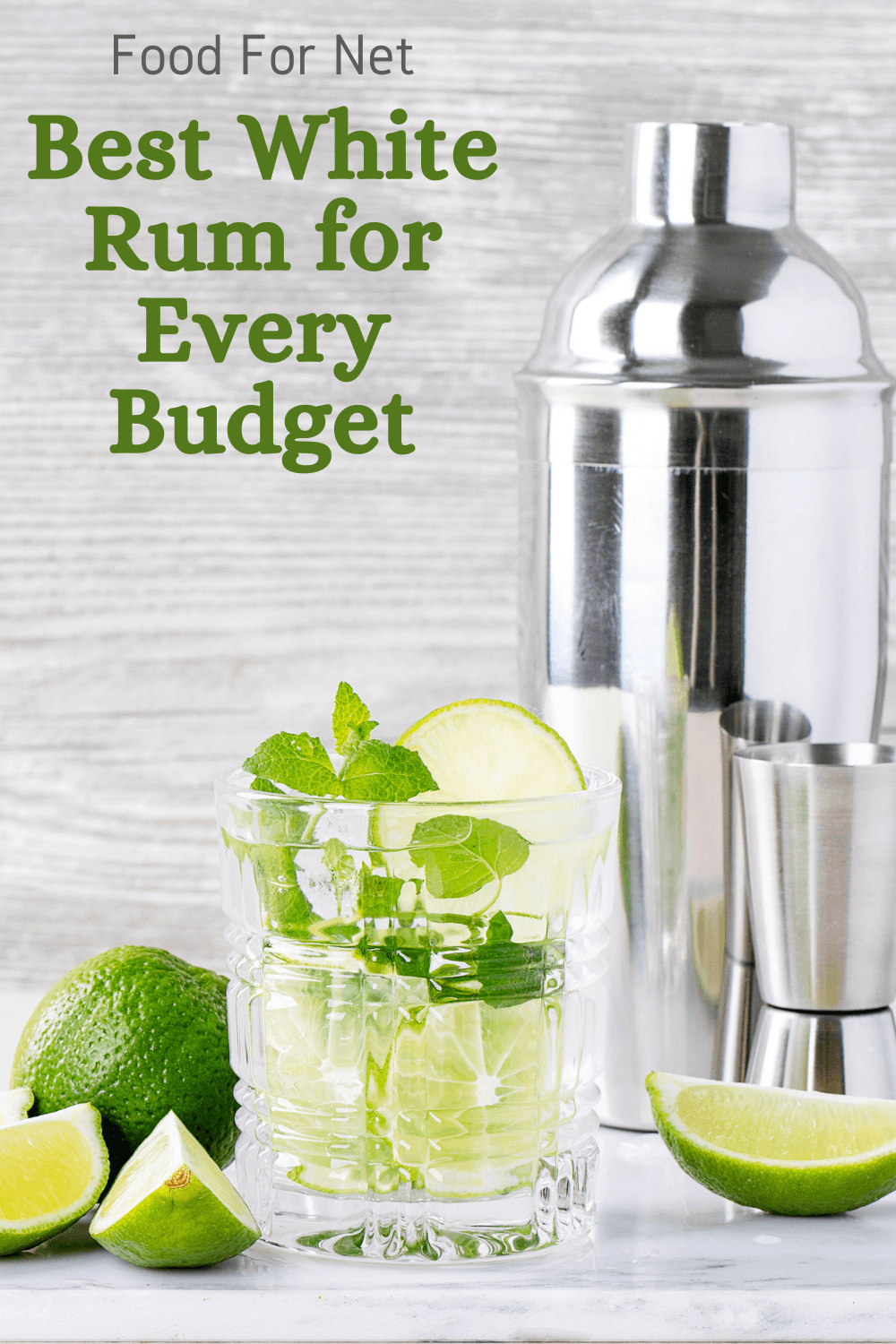 A mojito on the table, next to a jigger, a cocktail shaker, and some limes