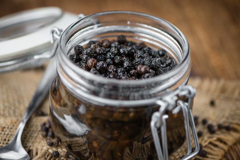 small spice jar full of black peppercorns resting on a piece of sack cloth with silver spoon beside it