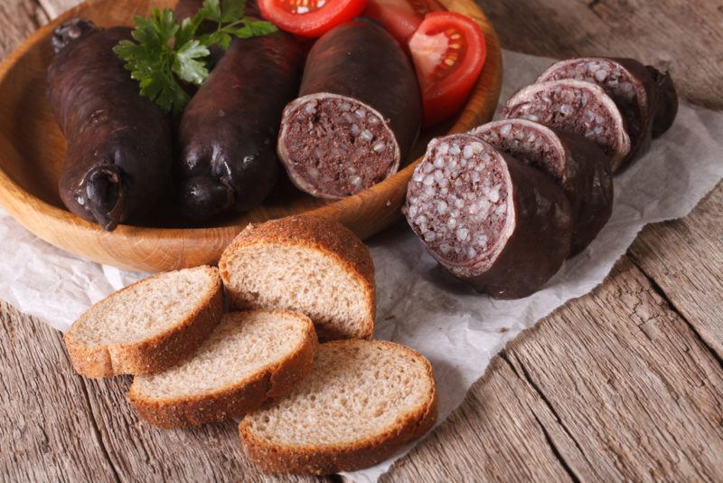 Various black puddings in a bowl, with a sliced black pudding and sliced bread on the table