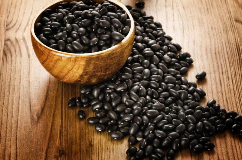 Black turtle beans on a table and in a wooden bowl