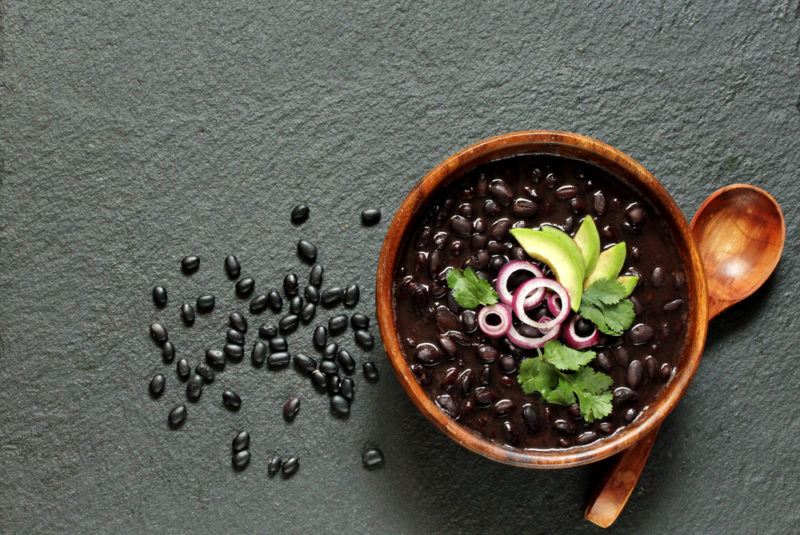 A bowl of black beans with more spilled onto the table