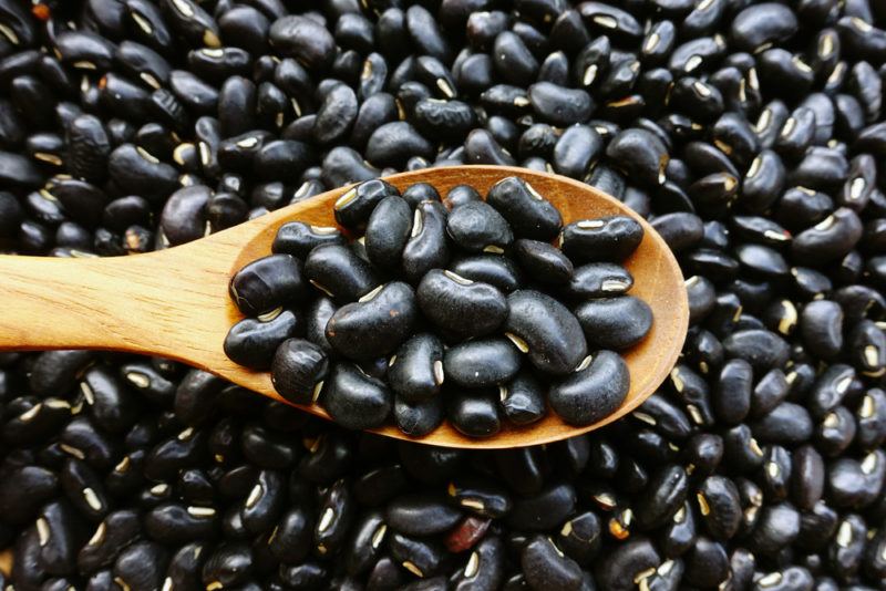 Black beans on a table and on a wooden spoon