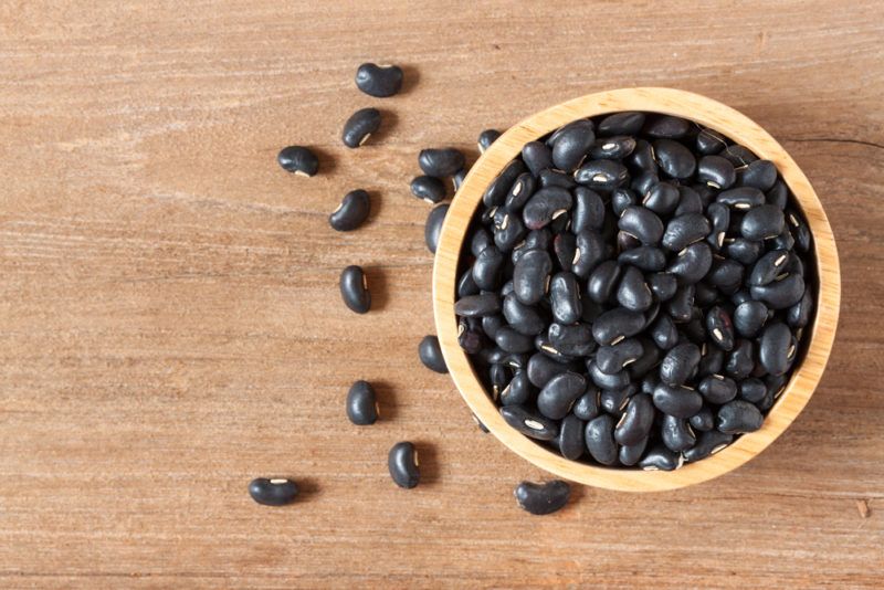 A wooden bowl containing black beans on a table