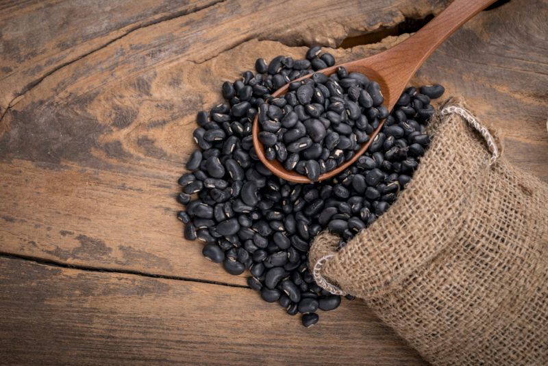 Black beans on a spoon spilling out of a bag on a wooden table