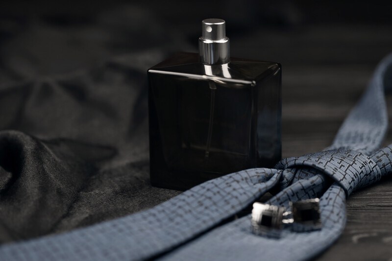 Black square bottle of cologne near a tie and shirt cuffs sitting on a black satin background