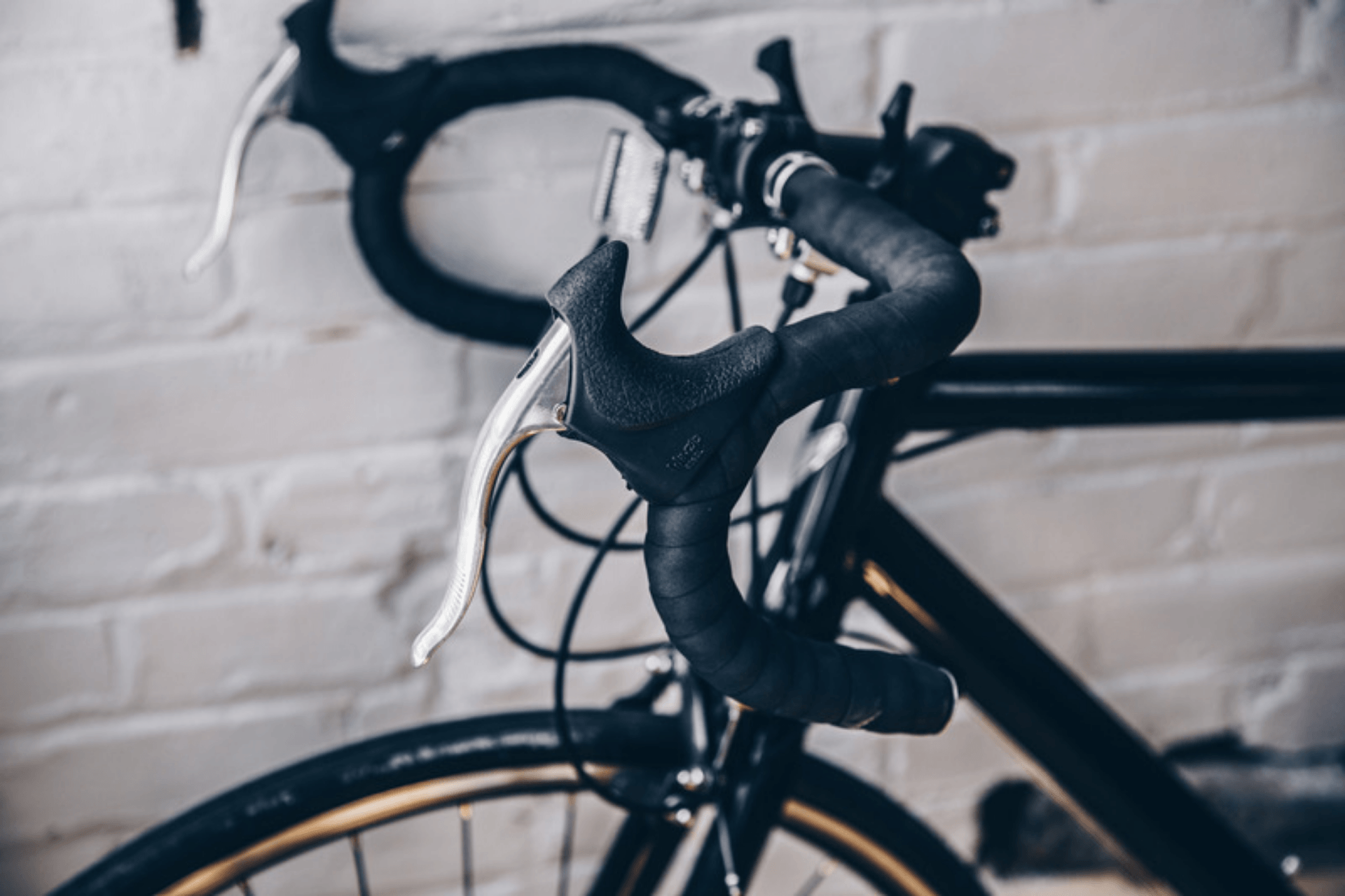 Black street bicycle with curved handlebars with gold rims and a white brick background