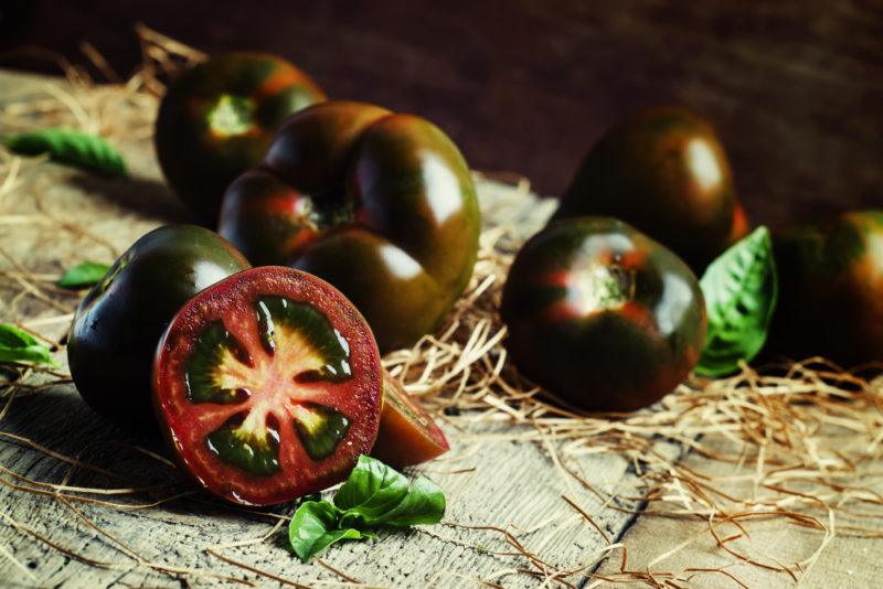 A collection of black tomatoes where one has been sliced open