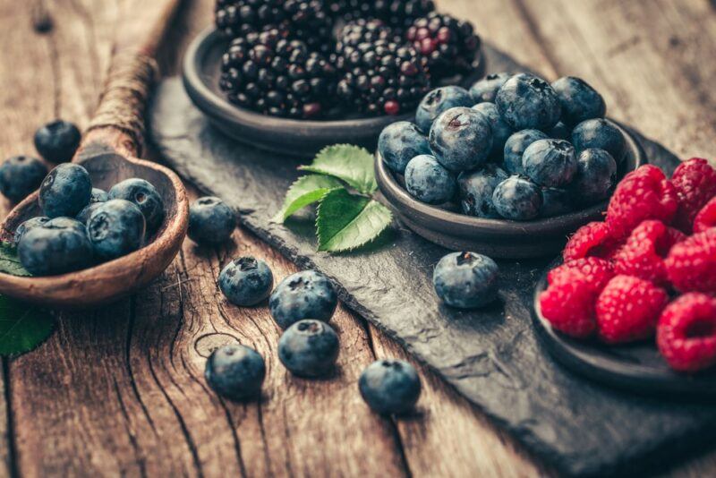 A rustic image showing four bowls of berries, including blueberries, blackberries, and raspberries