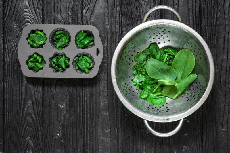 Blanched spinach in a strainer and muffin tins