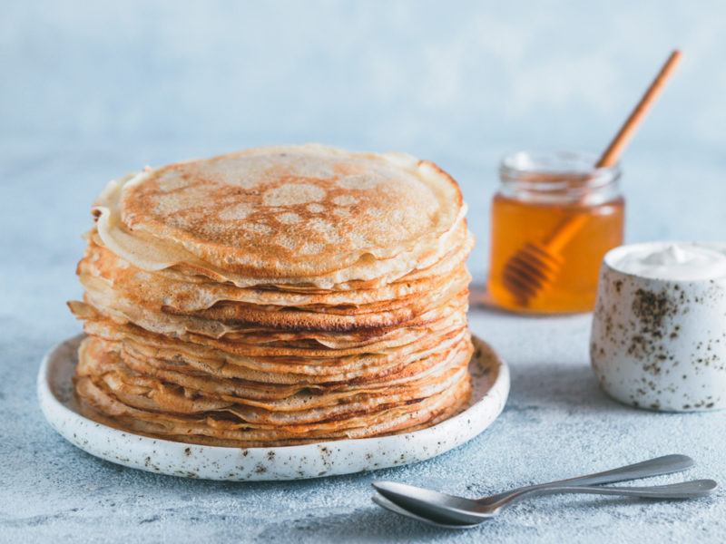 A stack of blini next to honey and yogurt