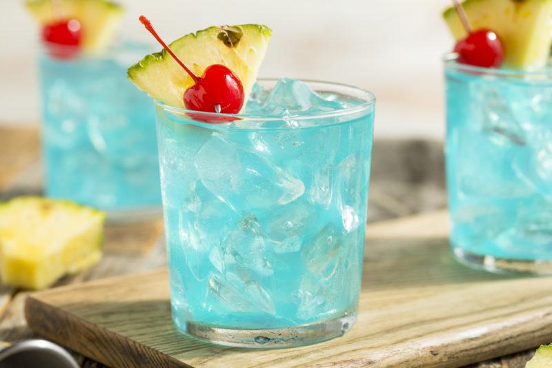 Three Blue Hawaiian cocktails with cherries and pineapple on a table