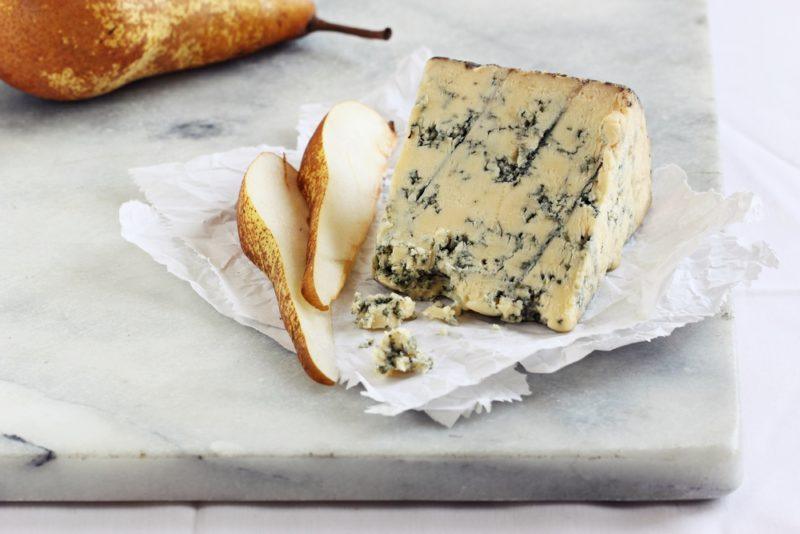 Blue Stilton cheese on a marble cutting board with pear