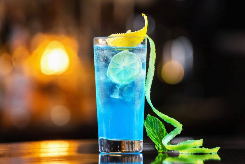 A Blue lagoon cocktail in a tall glass with an out-of-focus bar in the background