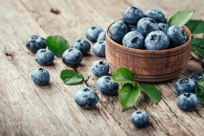 A small brown bowl of blueberries on a wooden table