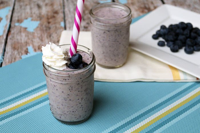 Two glasses of blueberry smoothie and some blueberries on a plate