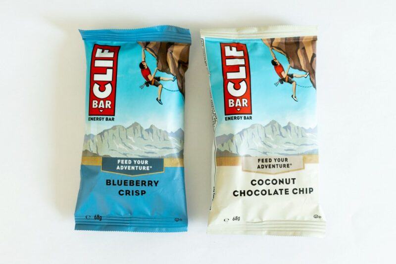 A blueberry crisp Clif bar and a coconut chocolate chip Clif bar against a white background