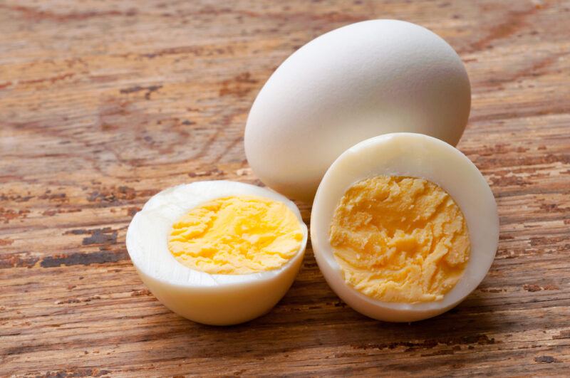 A whole egg and a boiled egg, cut in half, rest on a wooden surface.