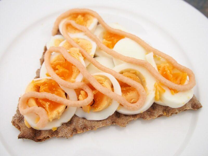 A piece of crisp bread with sliced boiled eggs and roe paste on a white plate