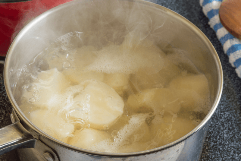 A stainless steel pot on the stove filled with potato pieces and boiling water