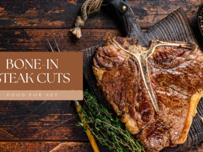 A porterhouse steak on a wooden table with a fork and some greens, highlighting the idea of bone in steak cuts