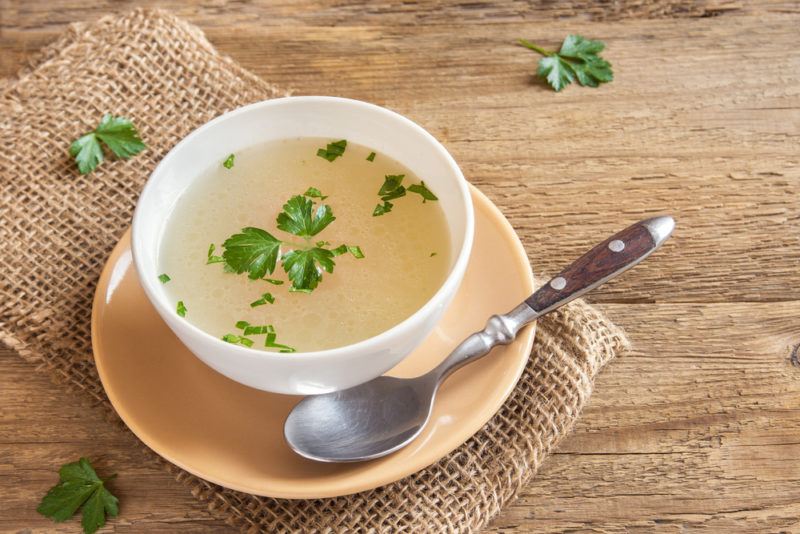 A whilte bowl containing bone broth with a saucer and a spoon