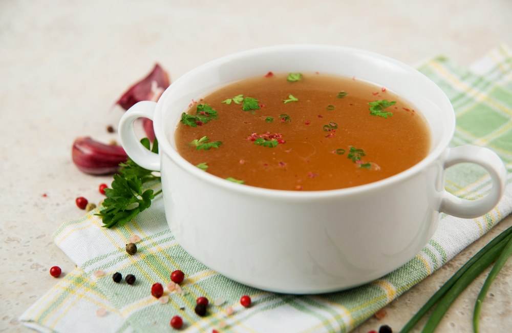 A white bowl with handles containing bone broth