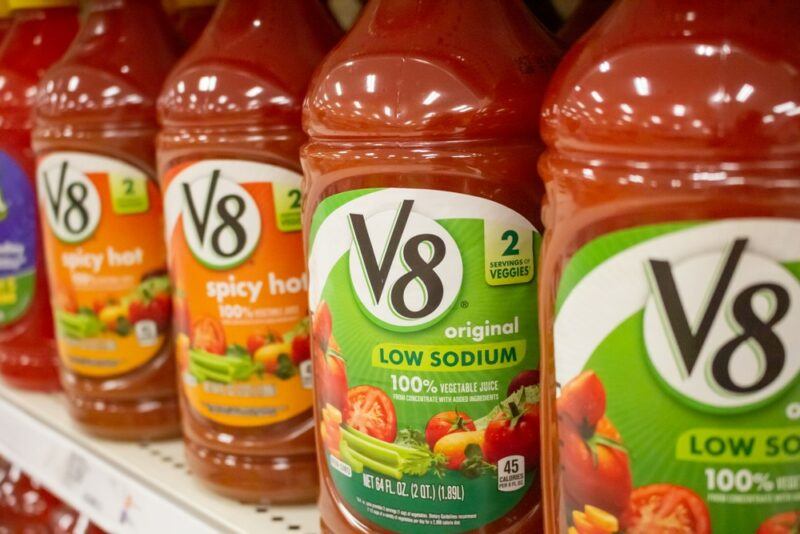 Bottles of V8 vegetable juice on a grocery store shelf, including the low sodium original version and spicy V8