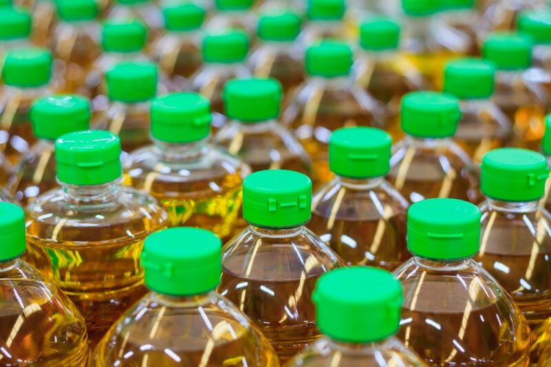 Many plastic bottles of canola oil with bright green lids