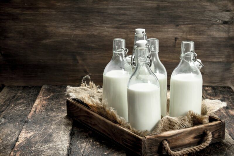 A wooden tray with four bottles of milk and a sack on a wooden floor