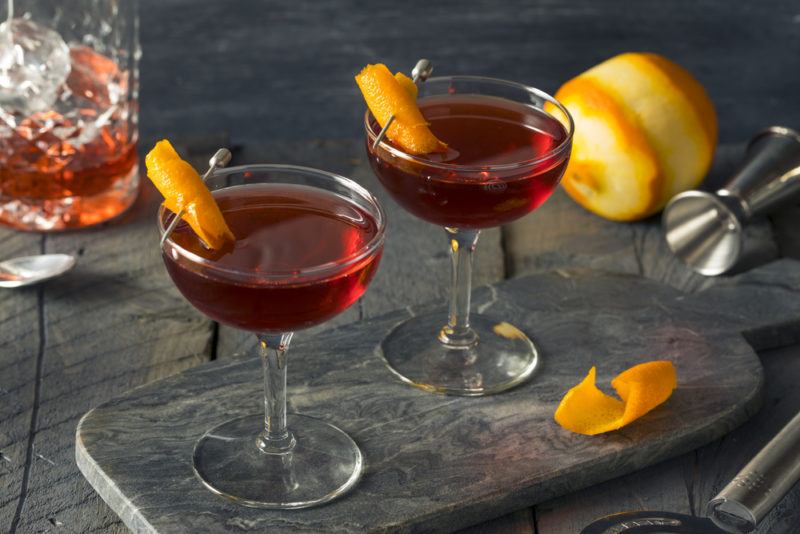 Two boulevardier cocktails on a slate next to an orange and a decanter