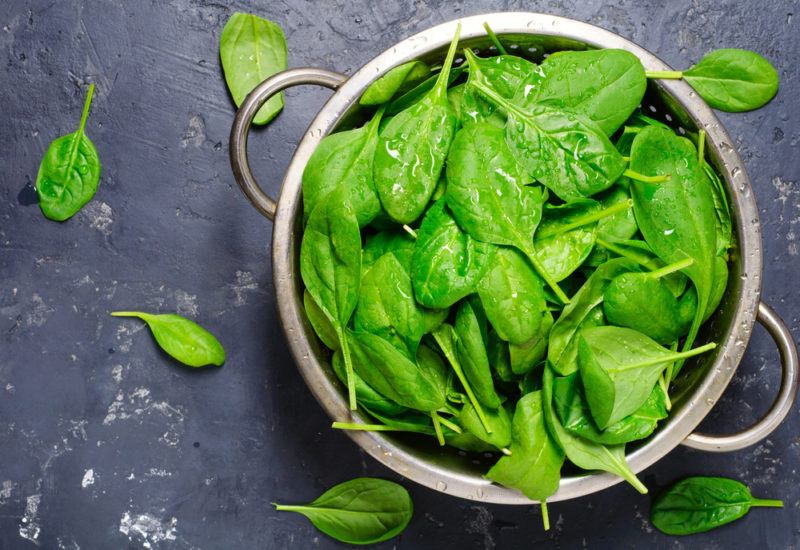 A bowl of spinach on a dark gray background